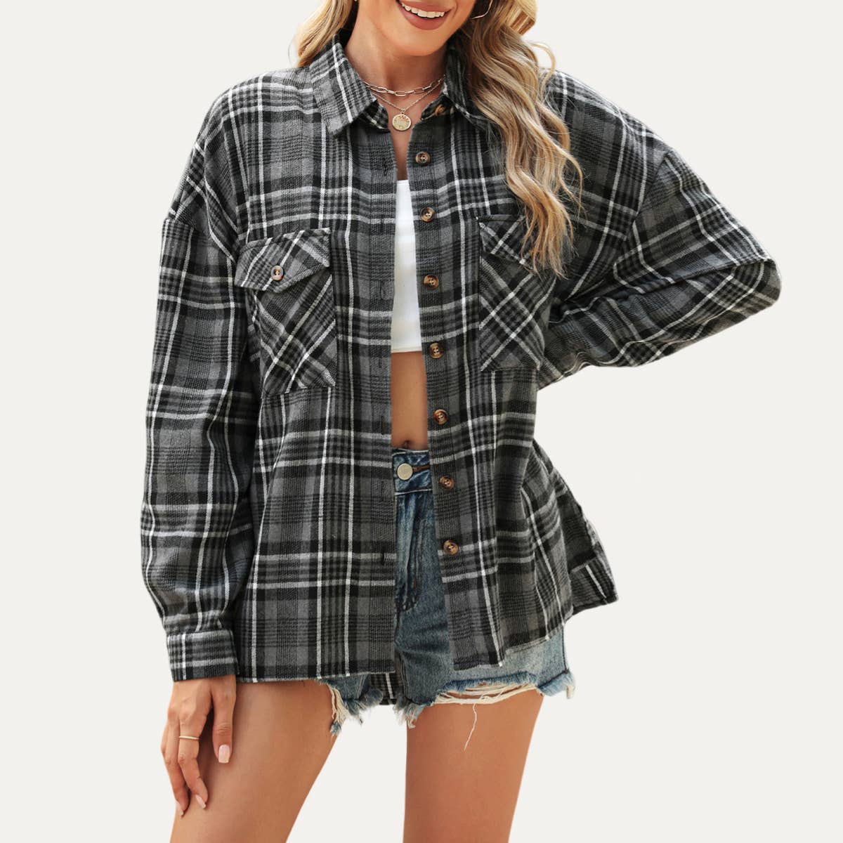Woman wearing a plaid shirt over a white top and denim shorts on a plain background
